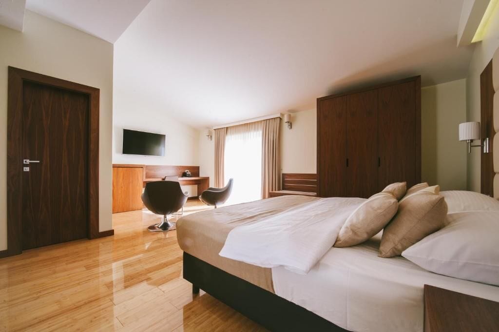A hotel room with a bed, a desk, a chair, a TV, and a wardrobe.