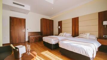 Ein Hotelzimmer mit Holzboden, zwei Betten, einem Holzschrank, einem Nachttisch, einem Sessel und einem kleinen Tisch mit Flasche und Gläsern.