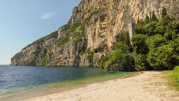 A coastal landscape with a rocky cliff, a clear beach, and a stone tower.