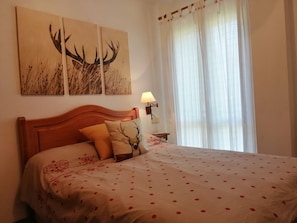 Un dormitorio con cabecera de madera, cama con colcha de lunares, dos cuadros en la pared de cuernos de ciervo, una lámpara de noche y cortinas de gasa.