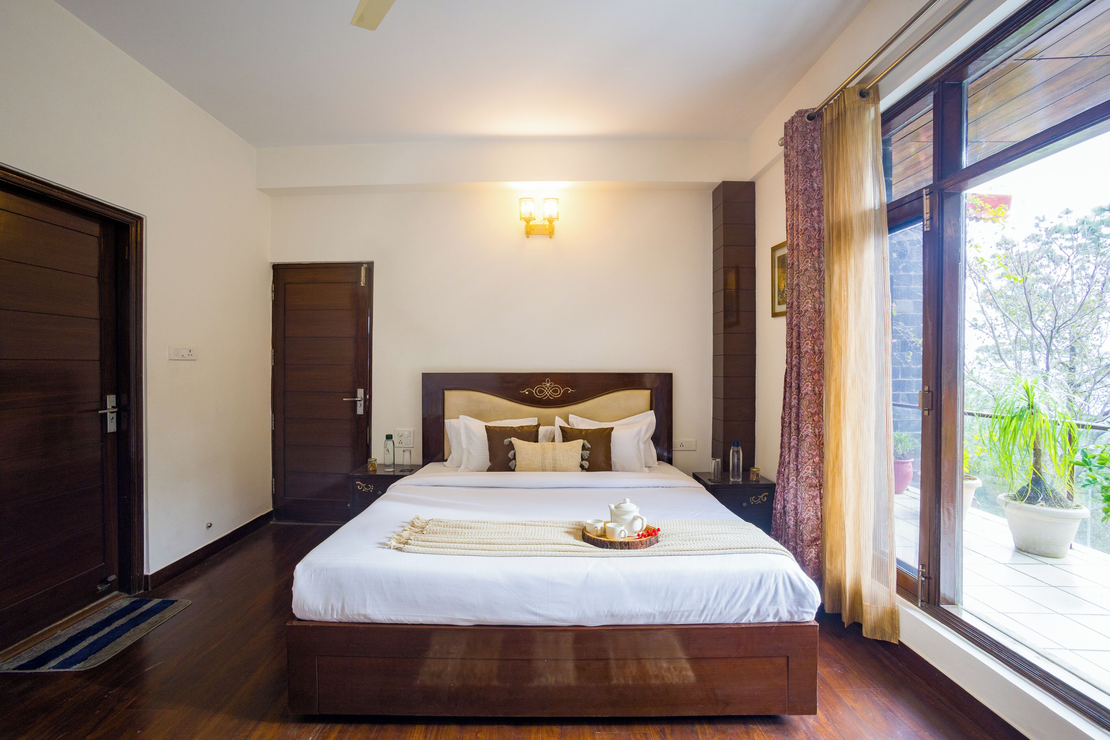 Une chambre d’hôtel avec un grand lit, une table de chevet, une lampe fixée au mur et une fenêtre avec des rideaux.