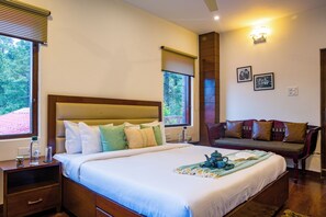 A neatly made bed with pillows, a bedside table with a bottle and glass, a sofa with cushions, and two windows with blinds. - Alaya Stays Kasauli Woods Cottage 3 BHK  (Kasauli)