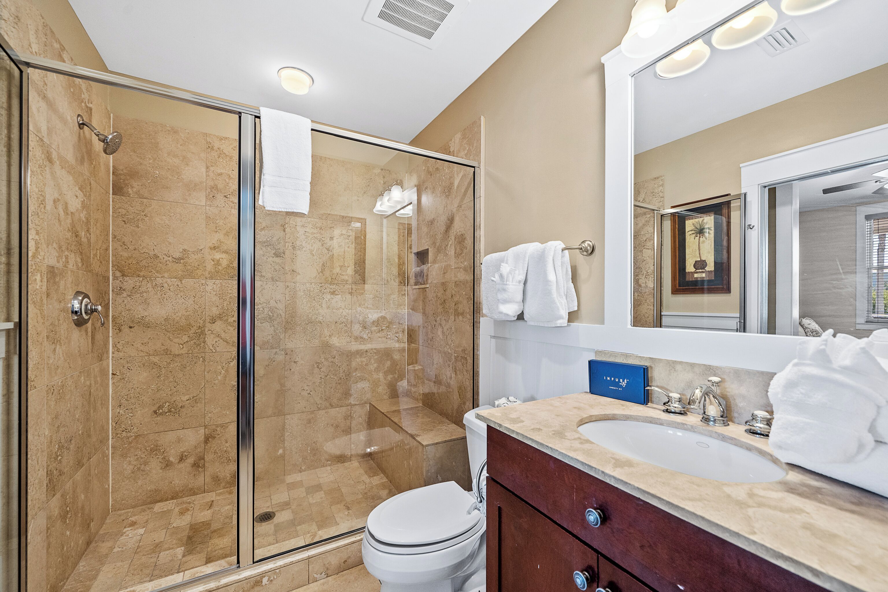 A bathroom with a glass-enclosed shower, a white toilet, a vanity with a sink, and a large mirror.