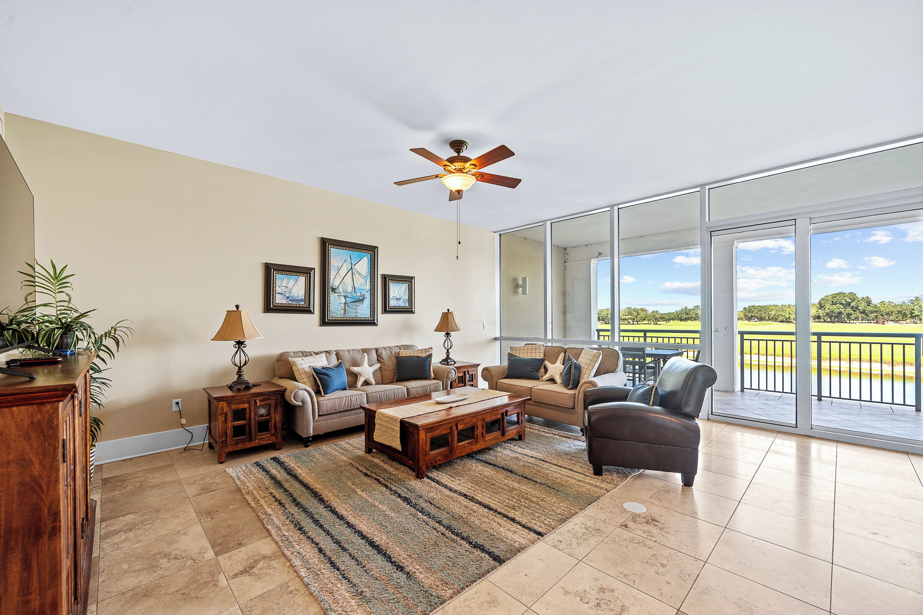 A spacious living room with a large window, a ceiling fan, and a view of a golf course.