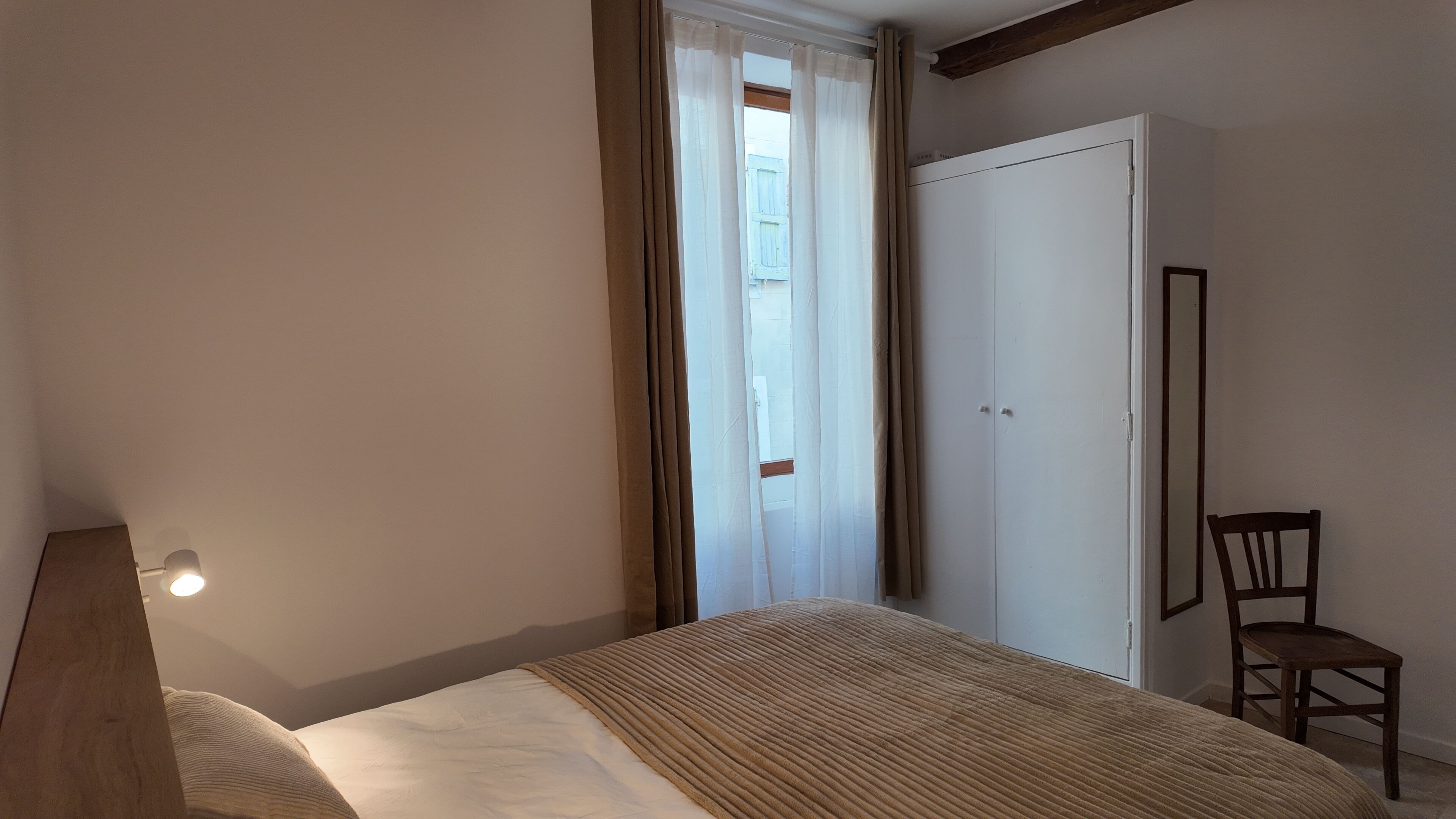 Una camera da letto con un letto, una sedia, un armadio e una finestra con tende.