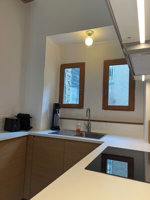 Una cocina moderna con lavavajillas integrado, cafetera y pileta. Hay dos ventanas que proporcionan luz natural.