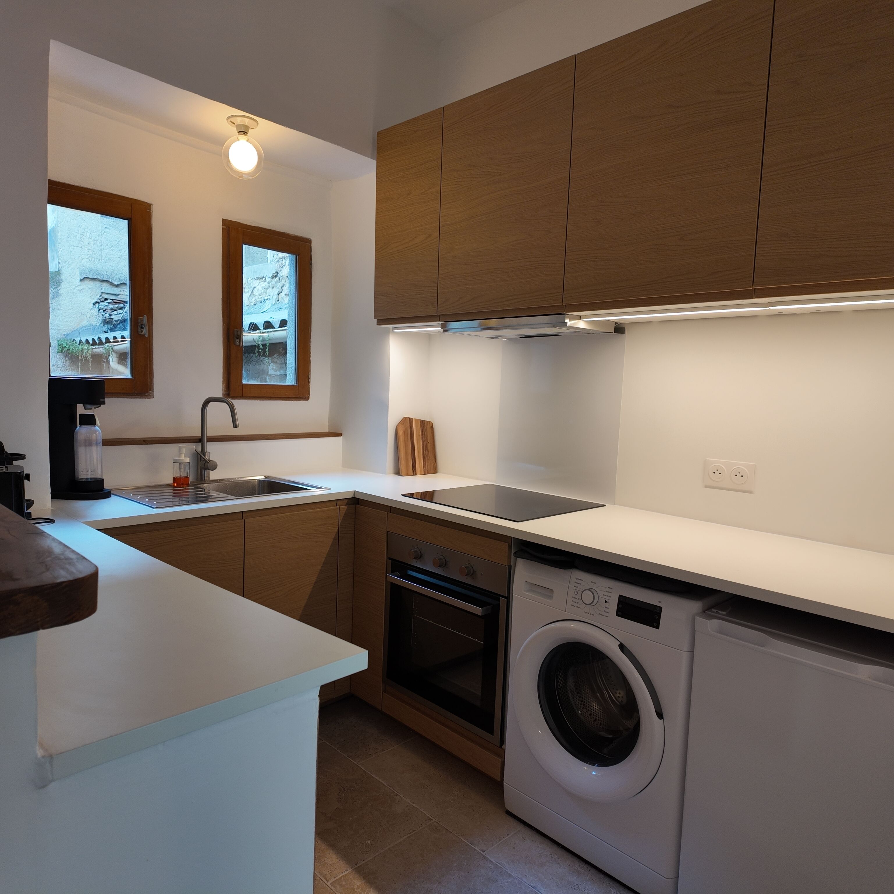 Una cocina compacta con armarios de madera, horno empotrado, lavadora y ventana con vistas.