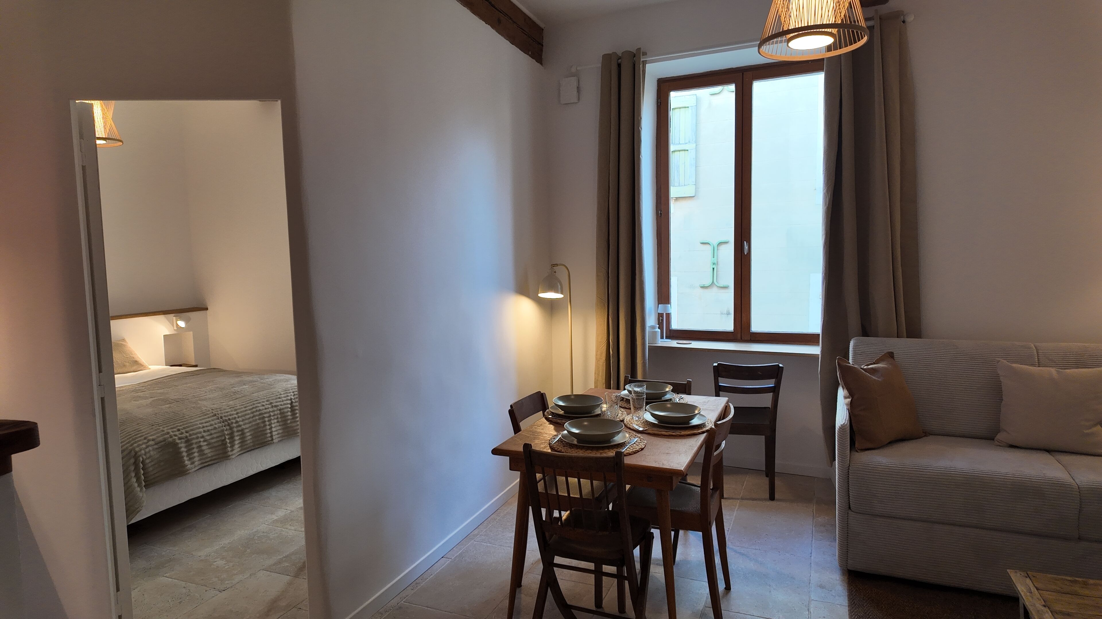 A cozy room with a bed, a dining table with chairs, a sofa, and a window with curtains.