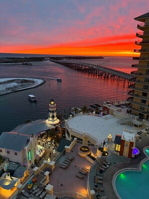 A resort with a pool, outdoor seating, and a view of the sunset over water. - Breathtaking Views Emerald Grande 3BR/2BA 904E (Destin)