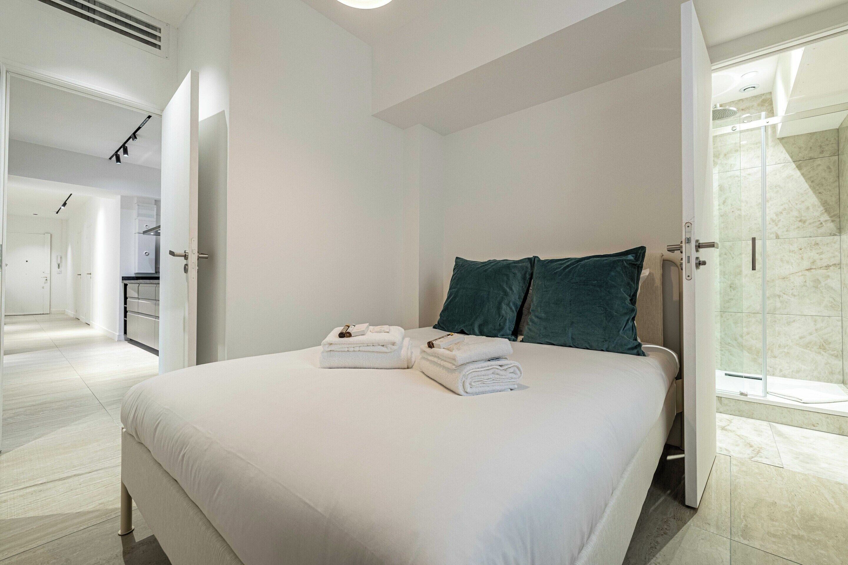 A modern hotel room with a large bed, two pillows, a neatly made bed, and a glass shower area.