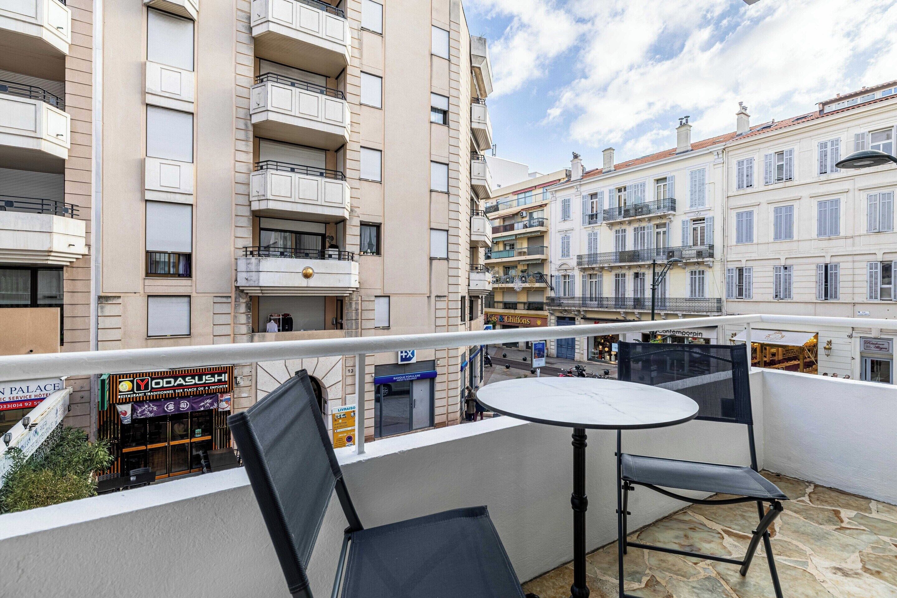 A balcony with a table and chairs, overlooking a street with buildings and a Yodashu sushi restaurant.