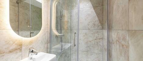 A modern bathroom with a glass-enclosed shower, a white sink, and marble walls.