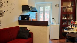 Een gezellige zithoek met een rode bank, een keuken met een ingebouwde kookplaat, een eettafel met een laptop en uitzicht door een glazen deur.
