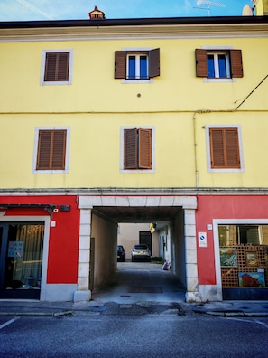 Un bâtiment jaune avec de nombreuses fenêtres, une entrée rouge et une voiture visible, garée dans la ruelle.