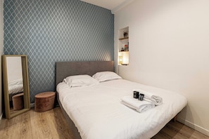 A neatly made bed with pillows, a bedside table with a lamp, a mirror, and a small stool. - Charming Apartment - AC- 1br/2p - Massena (Nice)