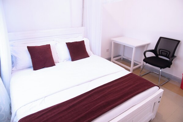 A bed with white bedding and a red blanket, a black chair, and a white bedside table. - LA FONT HOUSE Near JKIA (Nairobi)