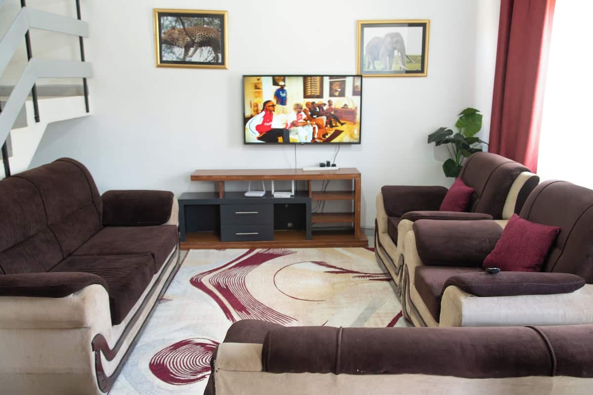 Una sala de estar con un sofá, un televisor de pantalla plana, una escalera y una planta.
