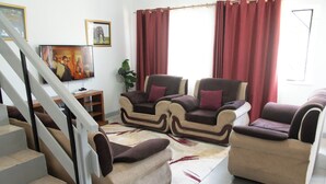 Una sala de estar con un conjunto de sofá, una televisión y una escalera.