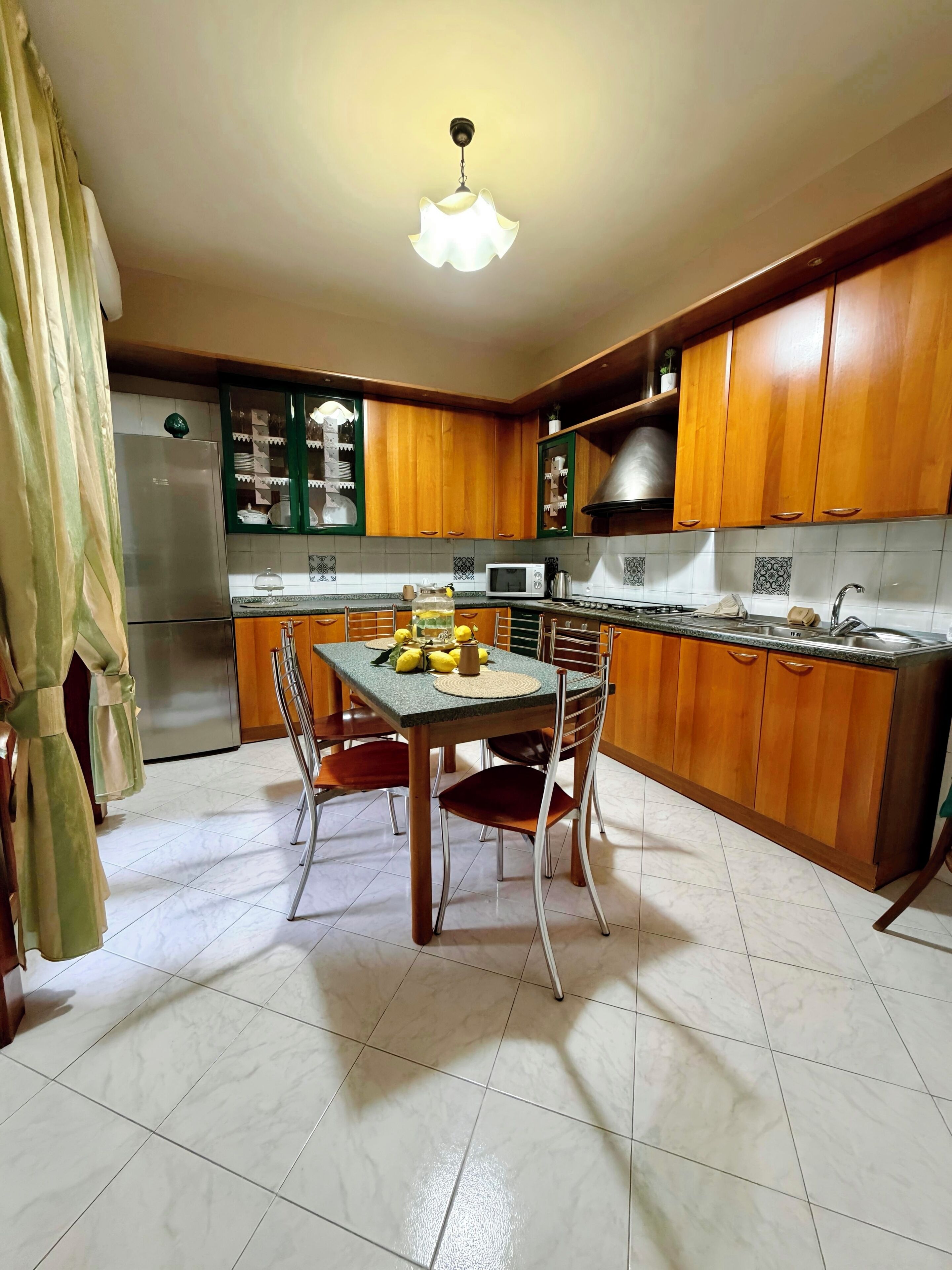 Una cocina con armarios de madera, una mesa de comedor con sillas, un refrigerador y un microondas.