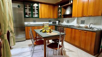 Una cocina con armarios de madera, una mesa de comedor con sillas, un refrigerador y un microondas.