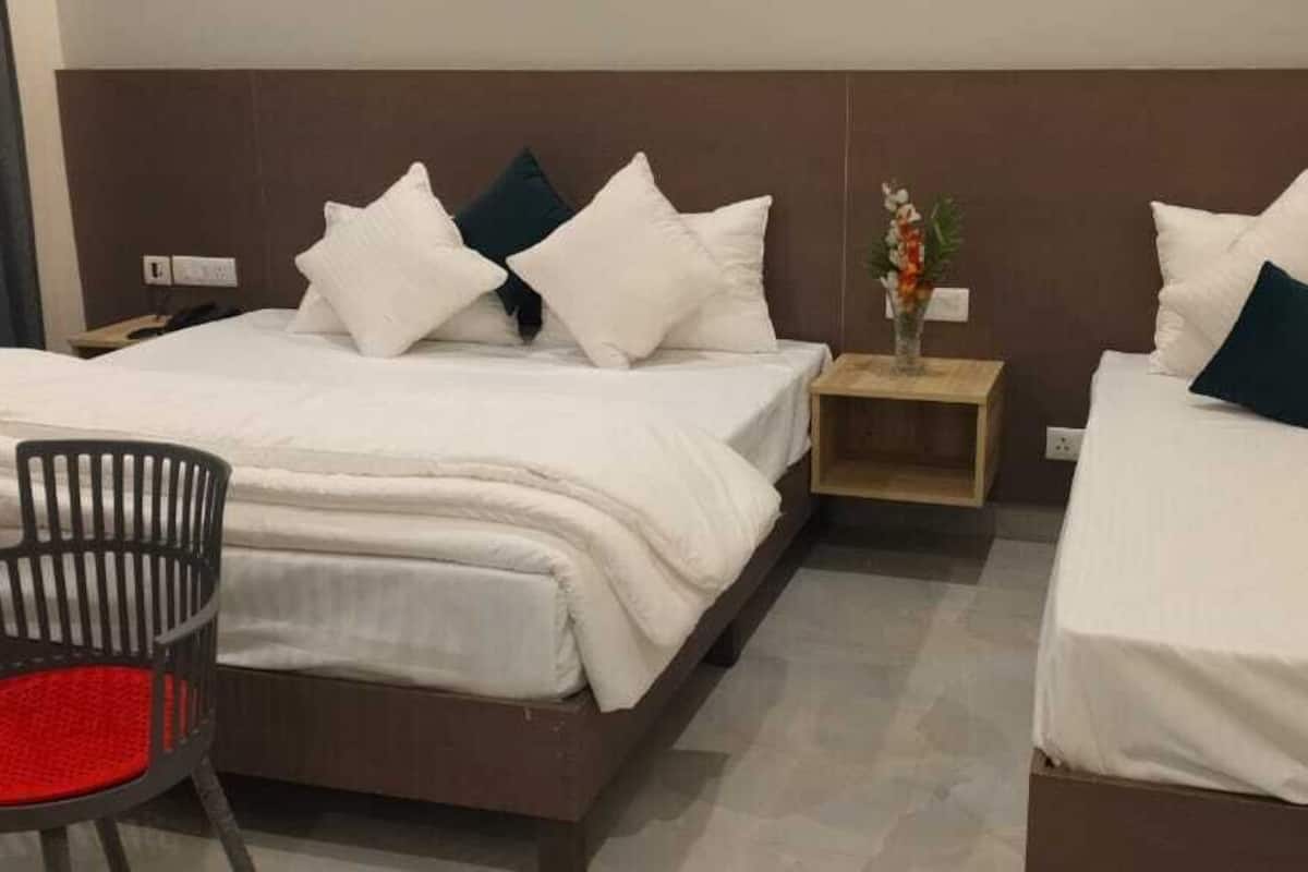 A hotel room with two beds, a small table with chairs, and a nightstand with a vase.