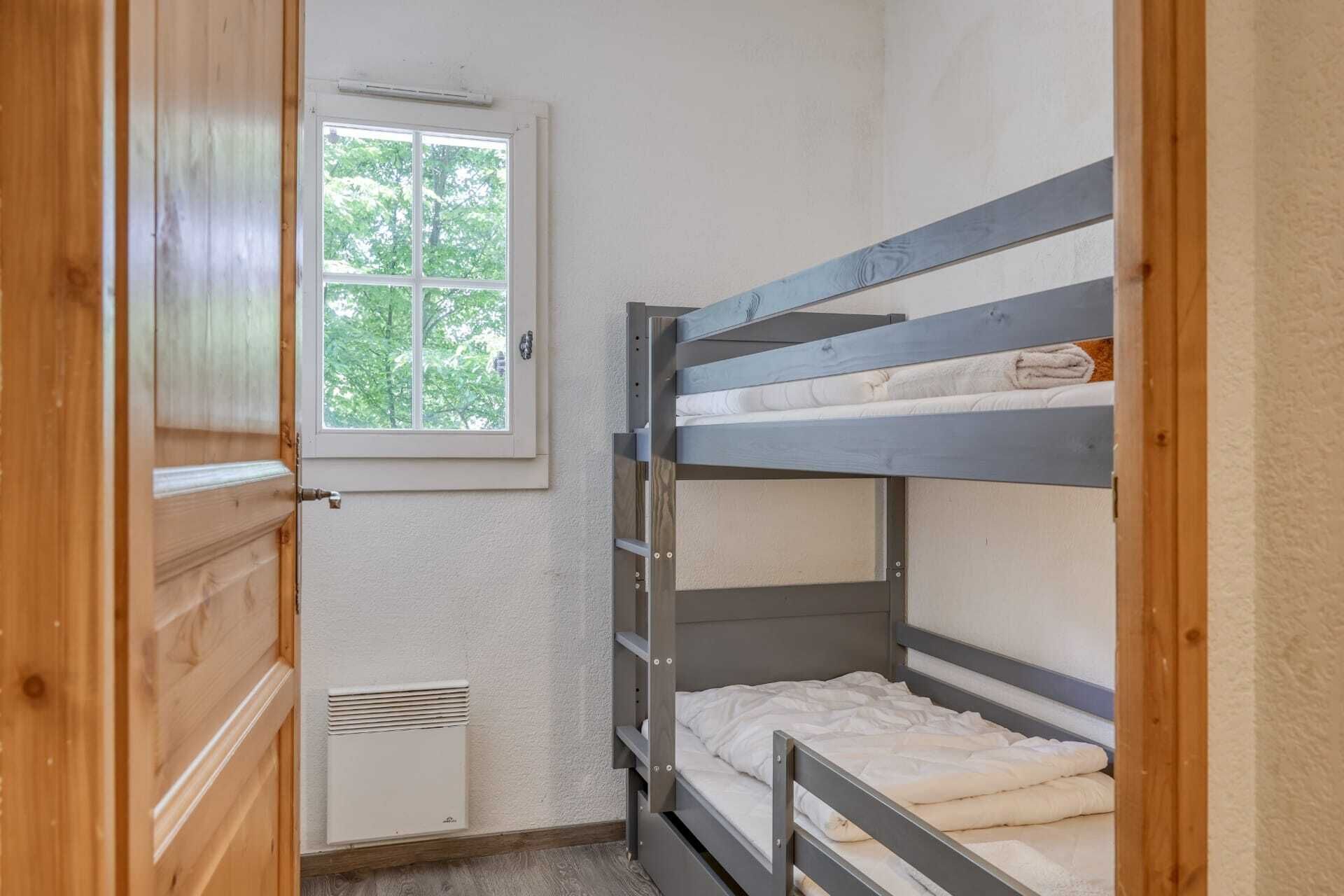 Habitación con literas, ventana, radiador y puerta de madera.