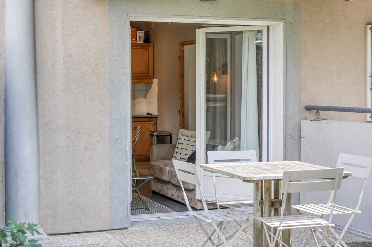 Een klein terras met een tafel en stoelen, een schuifdeur naar een keuken, en een witte muur.