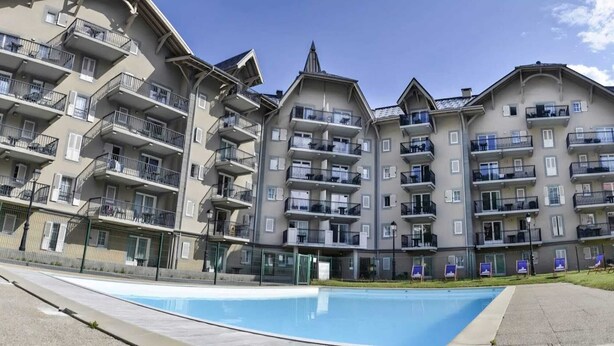 Un immeuble résidentiel à plusieurs étages, doté de balcons, d’une piscine et d’une entrée sécurisée.