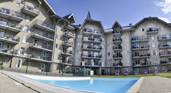 Un edifici residencial de diversos pisos amb balcons, una piscina i una entrada tancada per reixa.