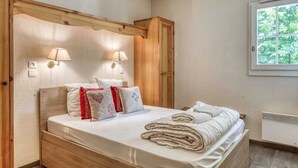 Une chambre à coucher avec une tête de lit en bois, deux lampes de chevet, un lit avec une literie blanche, une fenêtre donnant sur des arbres et un radiateur encastré.