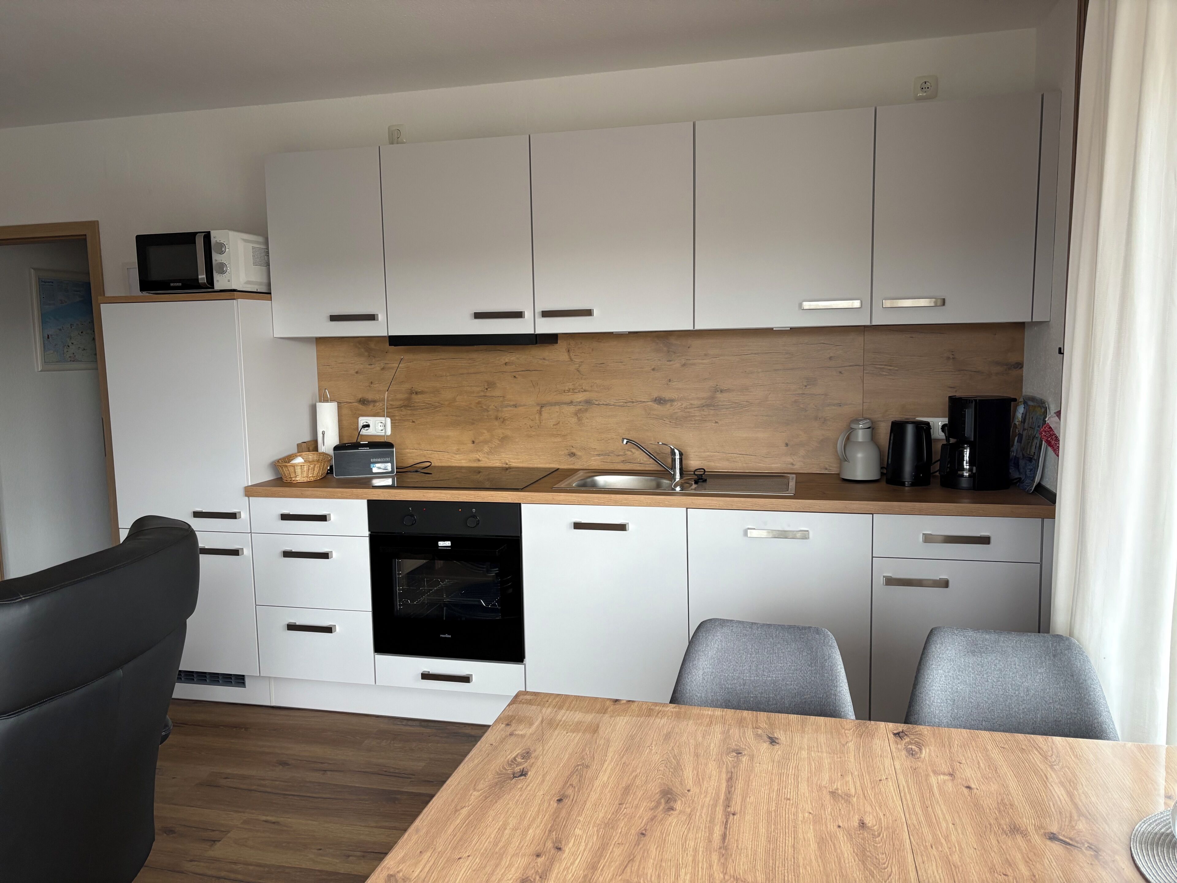 Une cuisine moderne avec des armoires blanches, un plan de travail en bois, un four encastré et un coin repas comprenant une table et des chaises.