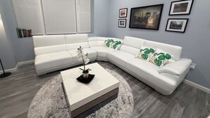 Een moderne woonkamer met een witte modulaire bank, een salontafel en een groot raam met zonwering.