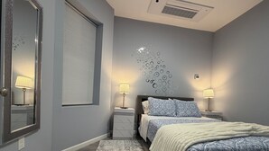 Een slaapkamer met een bed, twee nachtkastjes, een spiegel, een raam met zonwering en een decoratie aan de muur.