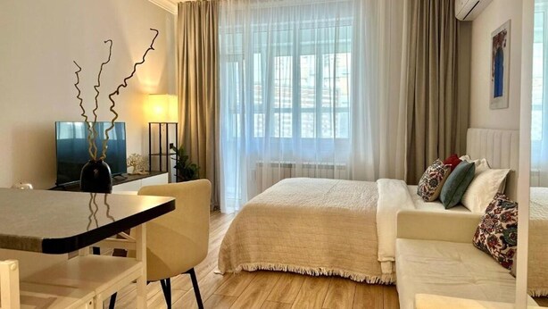 Ein Hotelzimmer mit Bett, einer Couch, einem Fernseher, einem Schreibtisch und einem Fenster mit Vorhängen.