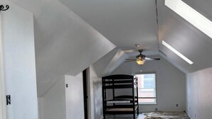 Ein Zimmer mit schrägem Dach, Deckenventilator und Fenster.