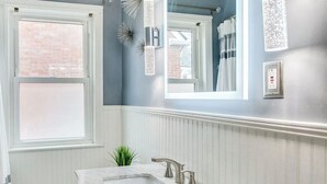 Un bagno con un mobile lavabo bianco, una finestra, uno specchio e applique decorative.