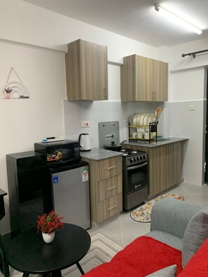 Eine kleine Küche mit Holzschränken, einem Kühlschrank, einem Herd und einer Mikrowelle.