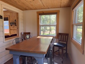 Un interior de madera con una mesa grande, sillas y un ventanal con vista al bosque.