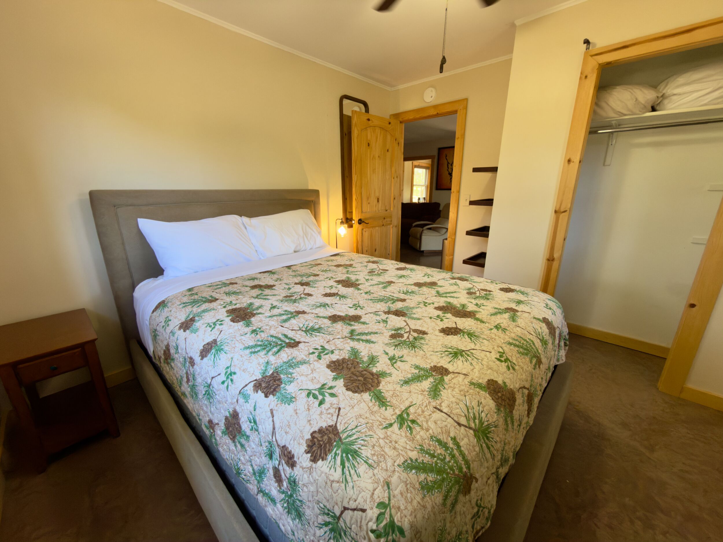 Un dormitorio con cama, mesita de noche, armario y puerta que da a otra habitación.