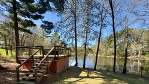 A wooden deck with stairs leading to a platform over a body of water, surrounded by trees.