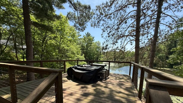 A wooden deck with a grill and seating area overlooking a body of water, surrounded by trees.