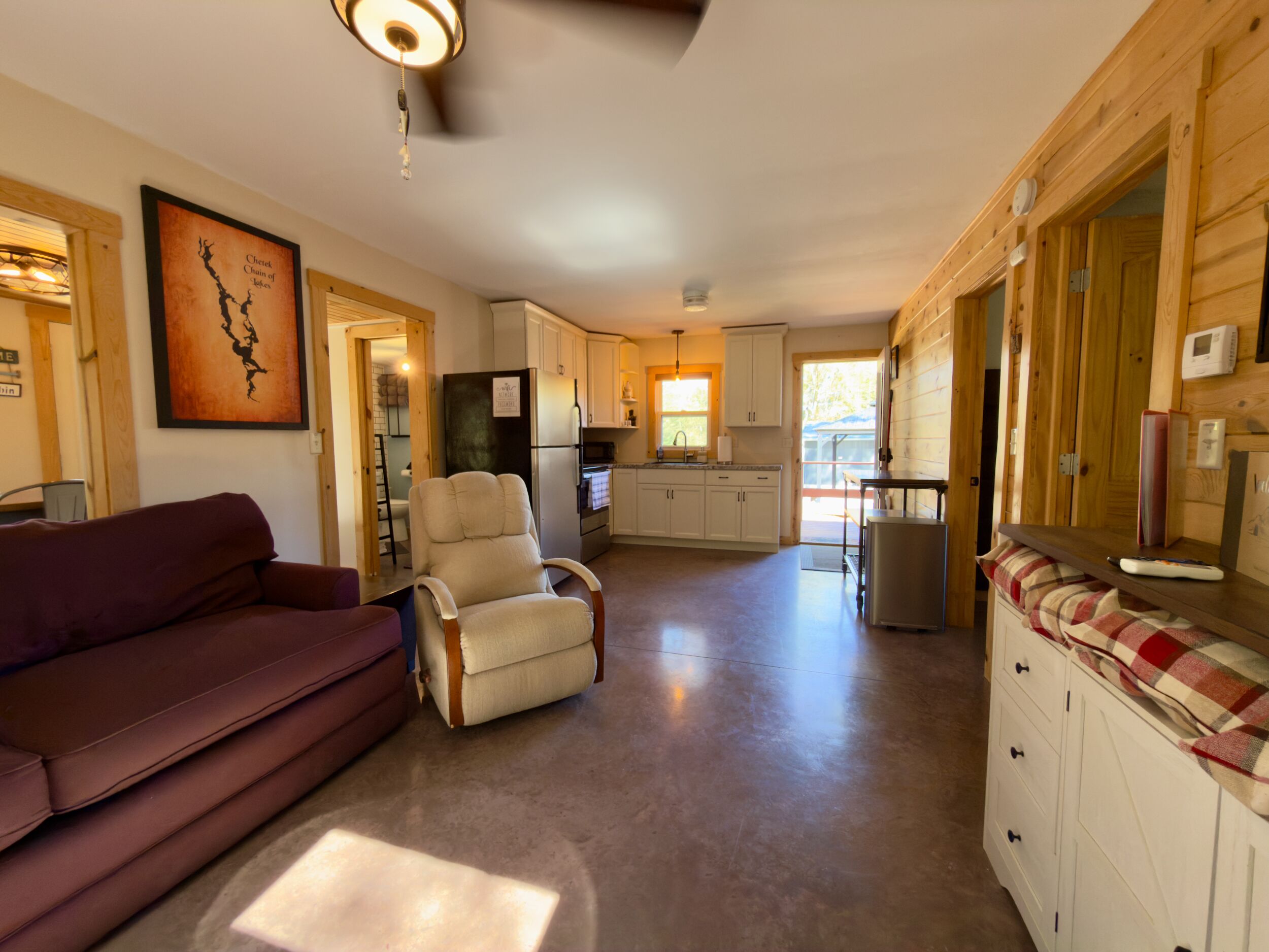 A spacious living area with a sofa, a recliner, a kitchen with a refrigerator, and wooden cabinets.