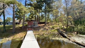 A wooden dock leading to a small cabin surrounded by trees and a body of water.