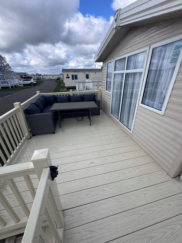 A covered outdoor deck with a sofa and a table, a white railing, and a view of a street and other buildings.