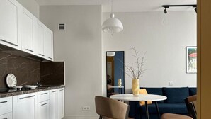 A modern kitchen with white cabinets, a marble countertop, and a dining area with a round table and chairs. - BSKYLINE bright 2-rooms apartment at vibrant area (Almaty)
