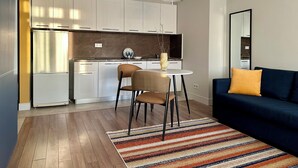 A modern kitchen with white cabinets, a dining area with a round table and chairs, and a dark blue sofa with a yellow pillow. - BSKYLINE bright 2-rooms apartment at vibrant area (Almaty)