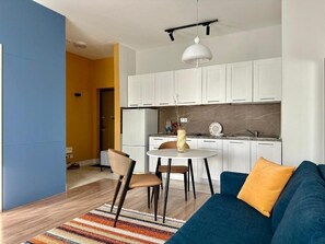 Una cocina moderna con armarios blancos, una mesa de comedor con sillas y un sofá azul con un cojín amarillo.