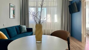 A modern living room with a sofa, a round table, and a vase with branches. - BSKYLINE bright 2-rooms apartment at vibrant area (Almaty)