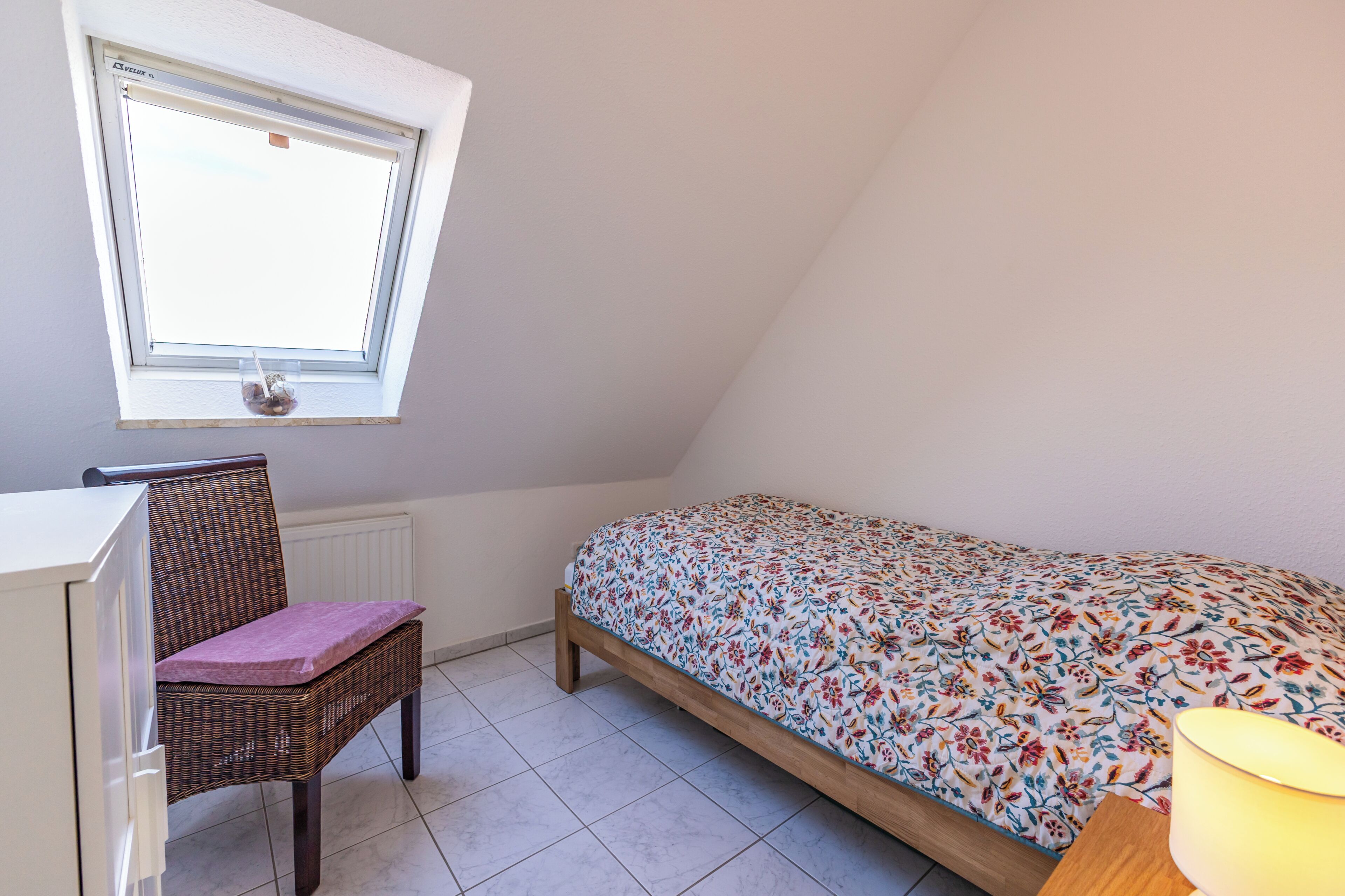 Ein Schlafzimmer mit Bett, Schreibtisch, Stuhl, Fenster und Lampe.