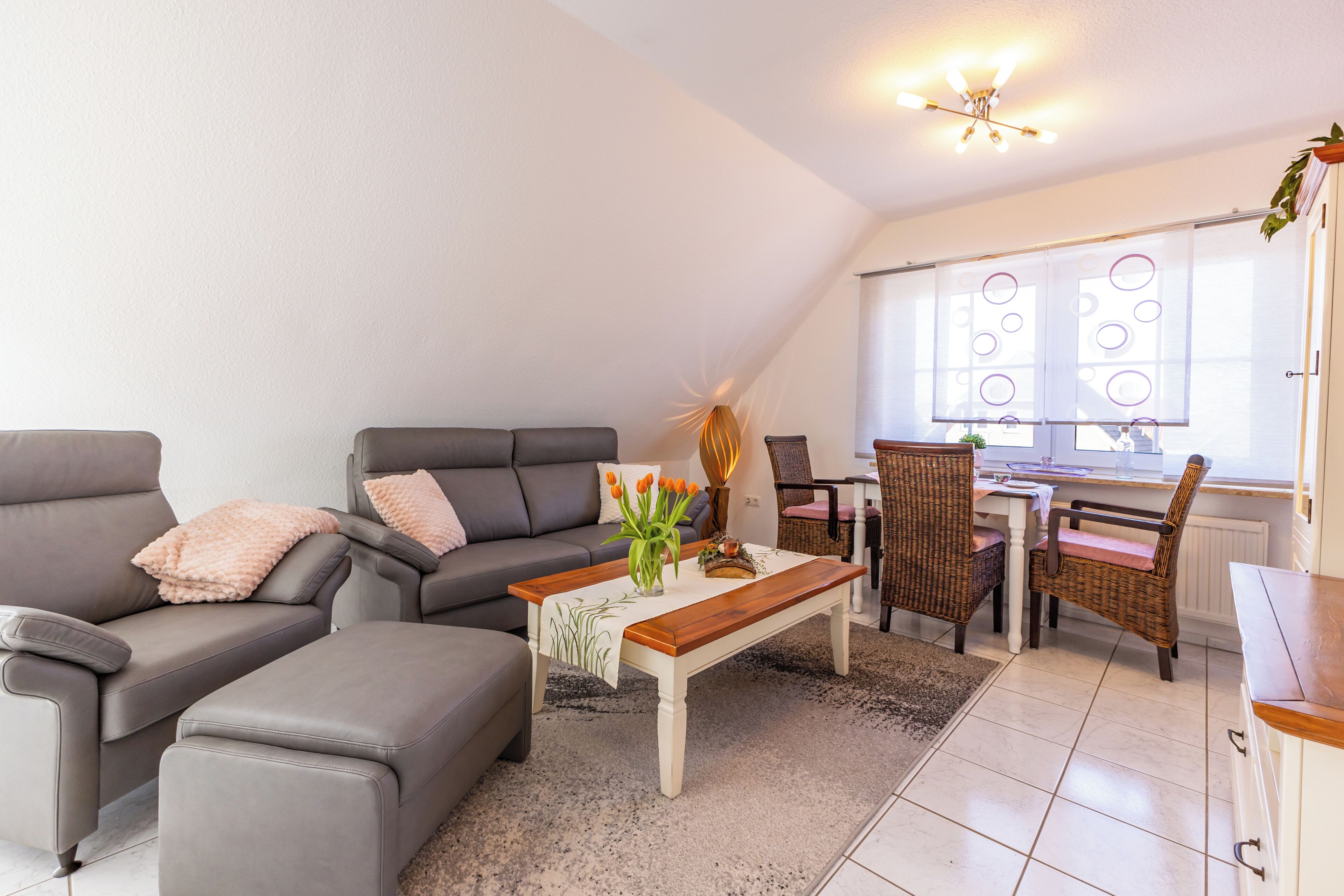 A modern living room with a grey sofa, a wooden coffee table, and a dining area with wicker chairs.